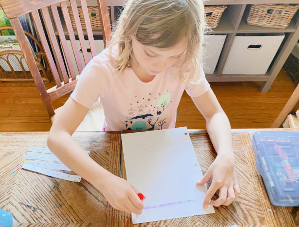 Child gluing the paper strips onto a piece of paper. They are glued in order.