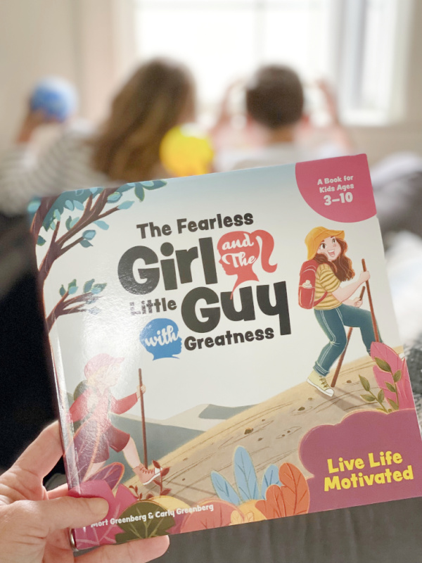 Two children blurred in the background with the book The Fearless Girl and The Little Guy with Greatness in the foreground.