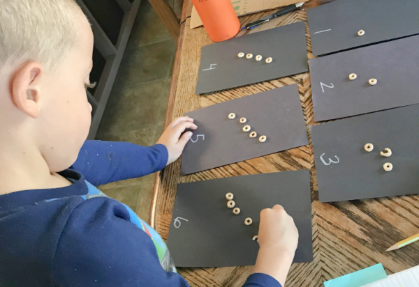 child counting cheerios onto labeled counting cards