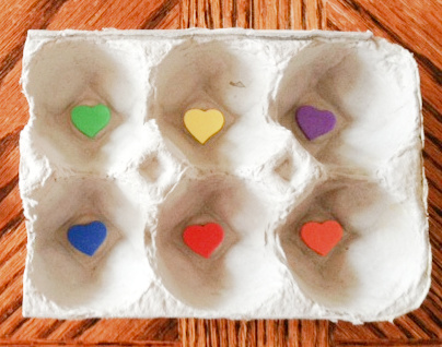 Egg carton cut in half. One colored sticker is stuck in the bottom of each egg cup. Green in one, purple in the other, and so on until there is one sticker in each cup, but all are different colors.