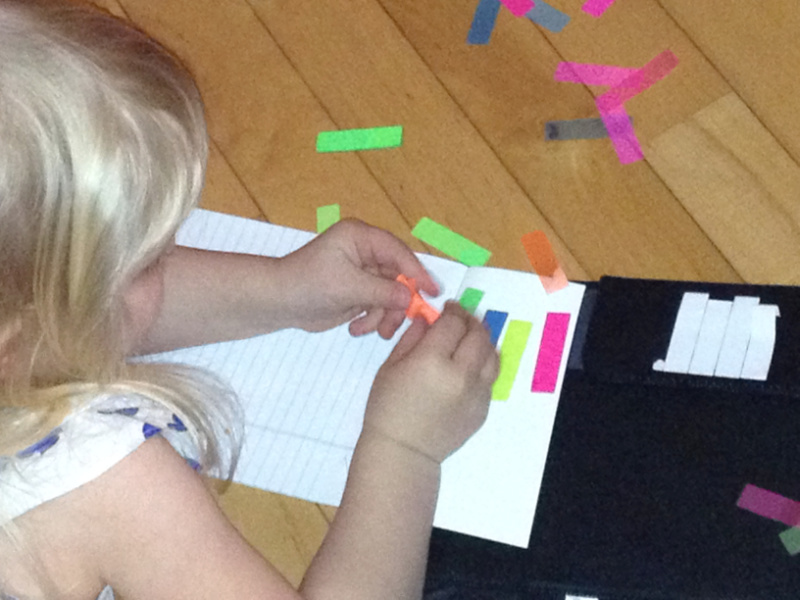 Toddler girl using fine motor skills to stick sticky tabs on paper.